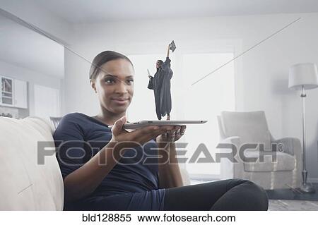 Stock Photography - Black woman watching figure of graduate standing on digital tablet. Fotosearch