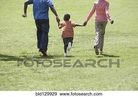 Stock Photo - Boy holding parents' hands in park. Fotosearch