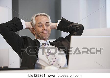 Businessman relaxing at desk in office View Large Photo Image Stock Image - Businessman relaxing at desk in office. Fotosearch