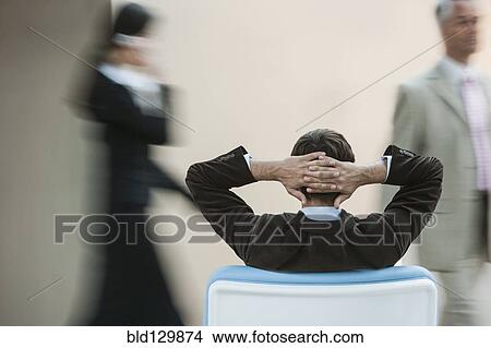Picture - Businessman relaxing in busy lobby. Fotosearch
