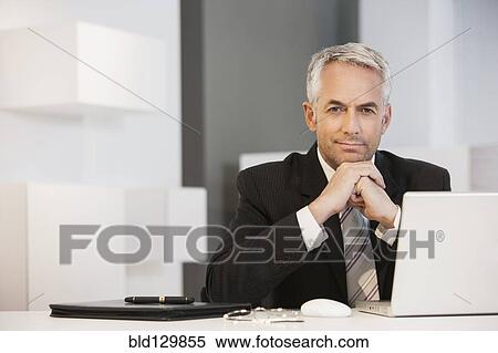 Businessman sitting at desk in office View Large Photo Image Stock Photography - Businessman sitting at desk in office. Fotosearch