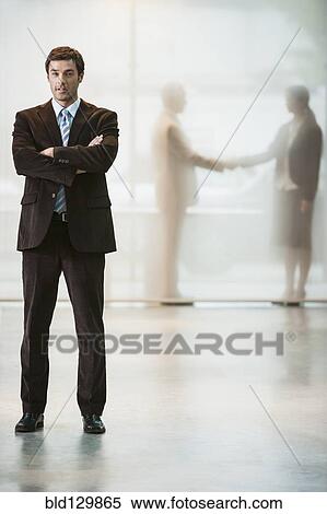 Businessman standing with arms crossed in office View Large Photo Image Stock Photography - Businessman standing with arms crossed in office. Fotosearch