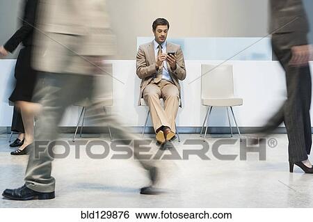 Stock Photograph - Businessman using cell phone in busy lobby area. Fotosearch