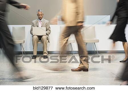 Stock Photo - Businessman using laptop in busy lobby area. Fotosearch