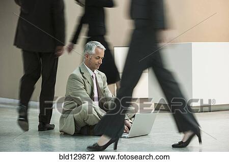Stock Image - Businessman using laptop on busy office floor. Fotosearch