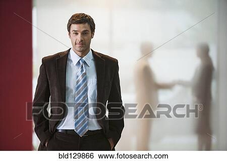 Stock Photograph - Businessman with hands in pockets in office. Fotosearch