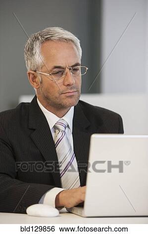 Businessman working at desk in office View Large Photo Image Stock Photograph - Businessman working at desk in office. Fotosearch
