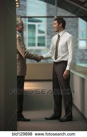 Stock Photo - Businessmen shaking hands in office. Fotosearch
