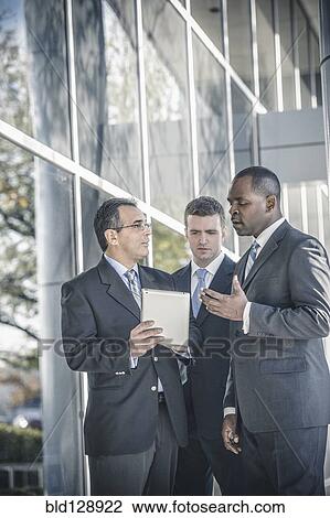 Stock Image - Businessmen using digital tablet outside office. Fotosearch