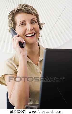 Stock Image - Businesswoman talking on phone in office. Fotosearch