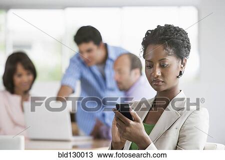 Stock Image - Businesswoman using cell phone in office. Fotosearch