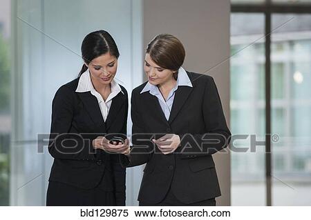 Stock Photography - Businesswomen using cell phone in office. Fotosearch