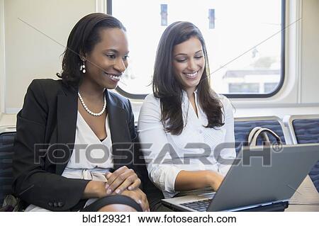 Stock Image - Businesswomen using laptop on train. Fotosearch