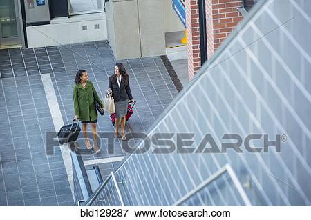 Stock Photo - Businesswomen with suitcases near escalator. Fotosearch