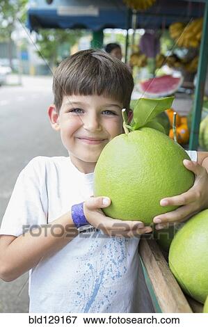 Stock Photo - Caucasian boy holding large fruit at market. Fotosearch