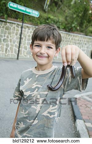 Stock Image - Caucasian boy holding millipede outdoors. Fotosearch