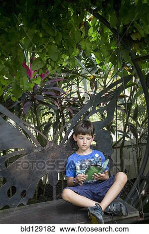 Stock Image - Caucasian boy reading on bench. Fotosearch