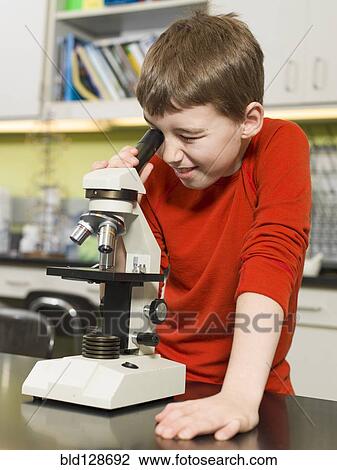 Stock Image - Caucasian boy using microscope in chemistry lab. Fotosearch