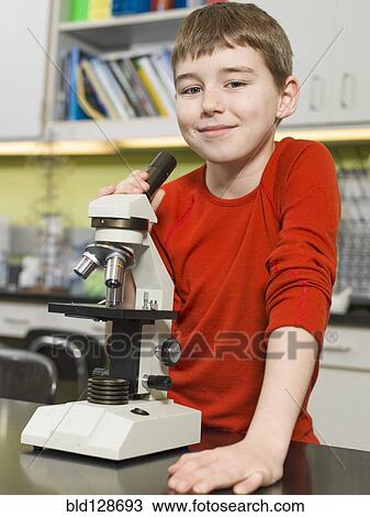 Stock Image - Caucasian boy using microscope in chemistry lab. Fotosearch
