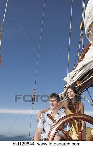 Picture - Caucasian couple at helm of sailboat. Fotosearch