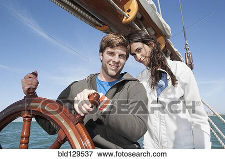 Stock Photo - Caucasian couple at helm of sailboat. Fotosearch