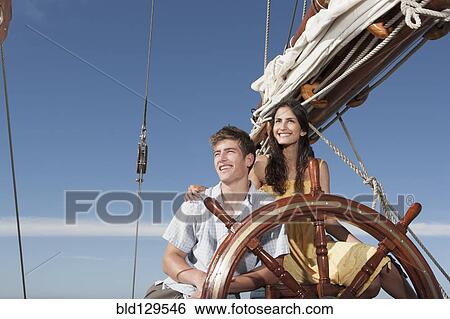 Stock Photograph - Caucasian couple at helm sailboat. Fotosearch