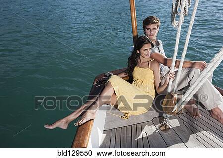 Stock Image - Caucasian couple relaxing on sailboat. Fotosearch
