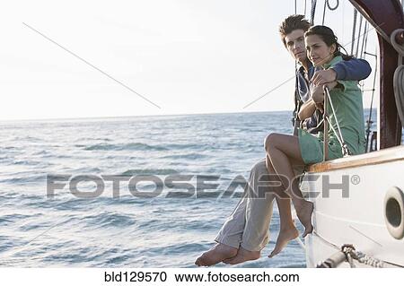 Stock Image - Caucasian couple relaxing on sailboat. Fotosearch