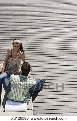 Stock Image - Caucasian couple relaxing on wooden dock. Fotosearch