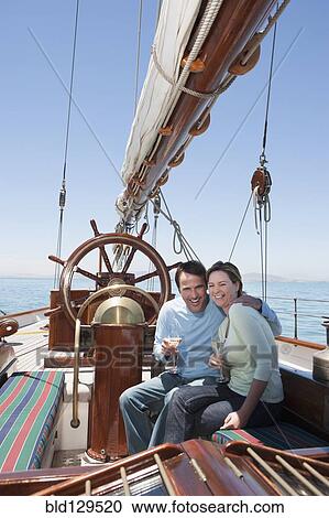 Stock Image - Caucasian couple toasting each other on sailboat. Fotosearch