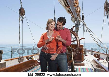 Stock Image - Caucasian couple toasting each other on sailboat. Fotosearch