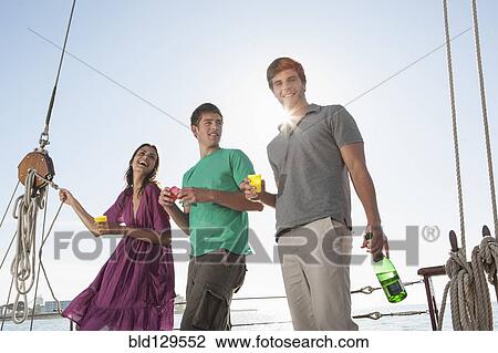 Stock Image - Caucasian friends laughing on sailboat. Fotosearch