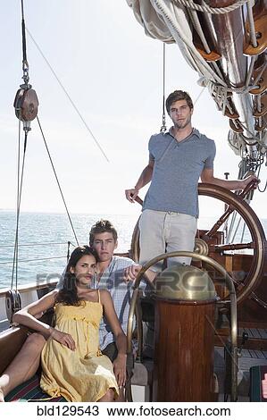 Stock Image - Caucasian friends relaxing on sailboat. Fotosearch