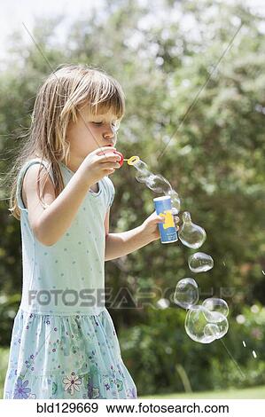 Stock Photo - Caucasian girl blowing bubbles outdoors. Fotosearch