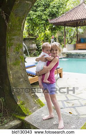 Stock Image - Caucasian girl holding baby brother in stone archway. Fotosearch