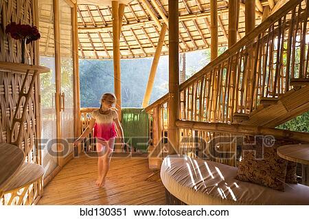Stock Image - Caucasian girl walking in bamboo living room. Fotosearch