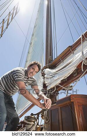 Caucasian man hoisting sail on sailboat View Large Photo Image Picture - Caucasian man hoisting sail on sailboat. Fotosearch