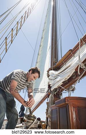Stock Image - Caucasian man hoisting sail on sailboat. Fotosearch