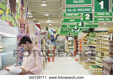 Stock Image - Caucasian man reading label in grocery store. Fotosearch