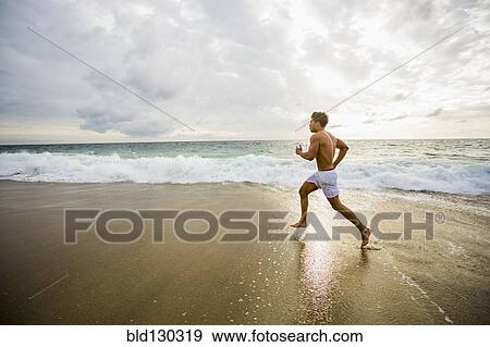 Stock Photo - Caucasian man running on beach. Fotosearch