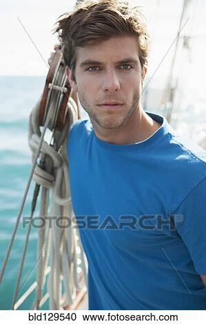 Stock Image - Caucasian man standing on sailboat. Fotosearch