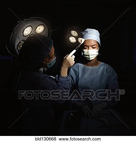 Stock Photo - Caucasian nurse wiping sweat from surgeon's brow. Fotosearch