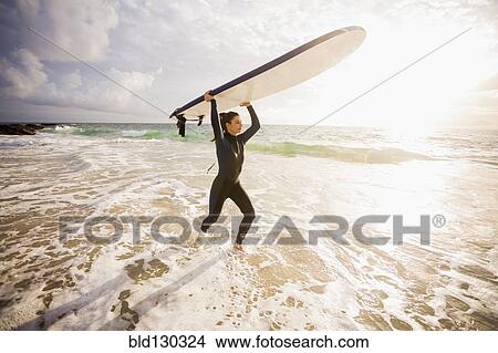 Caucasian surfer carrying board in waves View Large Photo Image Picture - Caucasian surfer carrying board in waves. Fotosearch