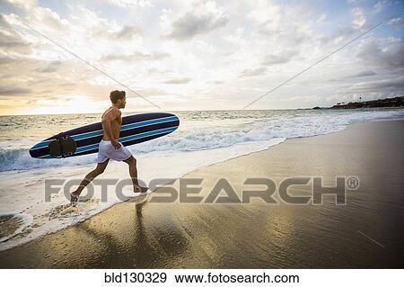 Caucasian surfer carrying board in waves View Large Photo Image Stock Photo - Caucasian surfer carrying board in waves. Fotosearch