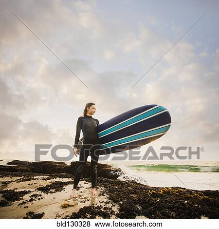 Stock Photo - Caucasian surfer carrying board on beach. Fotosearch