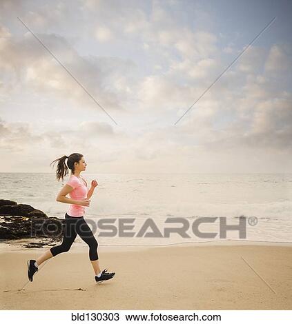 Stock Image - Caucasian woman running on beach. Fotosearch