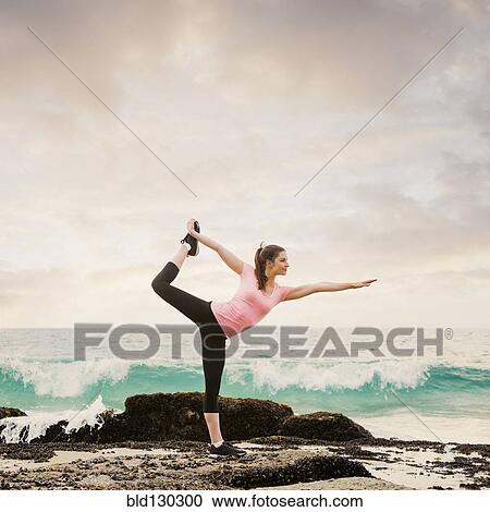 Stock Image - Caucasian woman stretching on beach. Fotosearch