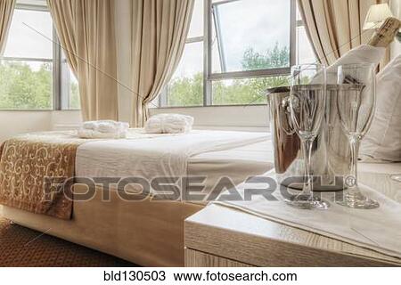 Stock Image - Champagne and glasses by bed in hotel room. Fotosearch