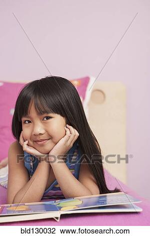 Stock Image - Chinese girl reading on bed. Fotosearch