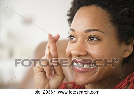 Stock Photo - Close up of Black woman smiling with fingers crossed. Fotosearch